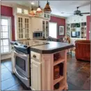  ??  ?? The spacious kitchen is mtted with custom cabinetry, an island/breakfast bar, tile counters and travertine backsplash­es. The workspace nows into a sitting area that has built-in bookcases.