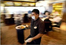  ?? DAVID J. PHILLIP — THE ASSOCIATED PRESS FILE ?? Marcelino Flores wears a face mask as he delivers food to a table at Picos restaurant in Houston in March.