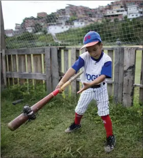  ?? ARIANA CUBILLOS — THE ASSOCIATED PRESS ?? In this photo, a boy swings a baseball bat using a donut to loosen his muscles during a practice session at the Brisas de Petare Sports Center in Caracas, Venezuela. More than 100 boys train daily on the baseball field using old bats, balls and gloves, in hopes of achieving a profession­al baseball career in the United States.