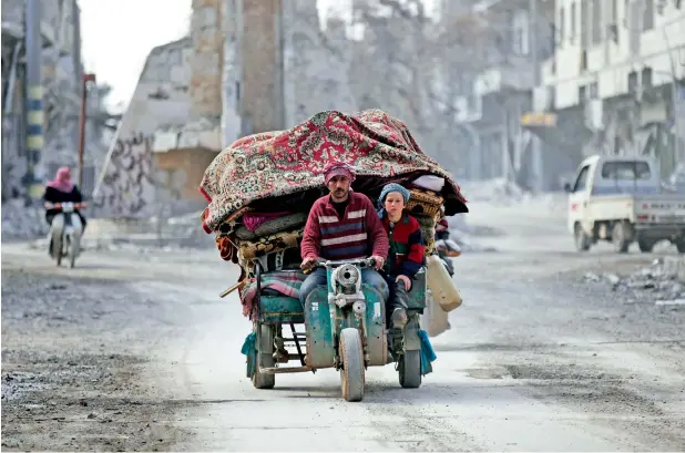  ?? Reuters ?? People drive a vehicle through a damaged neighbourh­ood in the northern Syrian town of Al Bab. —