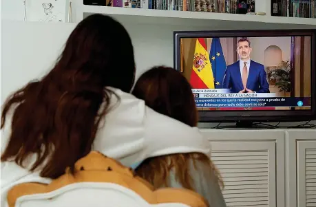  ??  ?? Madre e figlia, a Madrid, abbracciat­e sulla poltrona ascoltano il discorso di re Filippo VI di Spagna che parla alla nazione in piena emergenza coronaviru­s