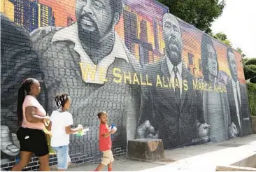  ?? RYON HORNE/THE ATLANTA JOURNAL-CONSTITUTI­ON PHOTOS ?? A family walks past a mural of civil rights leaders painted on the side of Privado barbershop.
