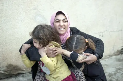  ??  ?? A woman holds her daughters as gunshots are heard in a neighborho­od liberated by Iraqi security forces in western Mosul. (AP)