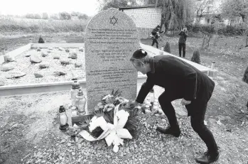  ?? CZAREK SOKOLOWSKI/AP ?? A man lays a candle last week at a memorial to some 60 Jews executed in 1942 in Wojslawice, Poland.