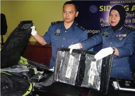  ??  ?? Excess baggage: Siti Baya (right) showing the seized drugs concealed in luggage at KLIA yesterday. Looking on is KLIA Customs officer Mohd Farhan Izhar.