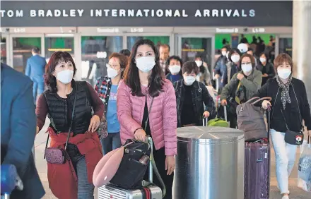  ?? MARK RALSTON/ AFP VIA GETTY IMAGES ?? Passengers wear protective masks as they arrive on a flight from Asia at Los Angeles Internatio­nal Airport. Health authoritie­s are concerned about a new coronaviru­s that has killed more than 130 people.