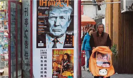  ??  ?? A man pushing a stroller past a magazine advertisem­ent featuring US President Donald Trump at a news stand in Shanghai, China, on Wednesday. Trump is hosting Chinese President Xi Jinping in Palm Beach, Florida, next month.