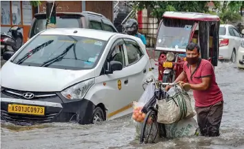  ?? — PTI ?? Commuters wade through a waterlogge­d street following heavy rainfall in Guwahati on Tuesday.