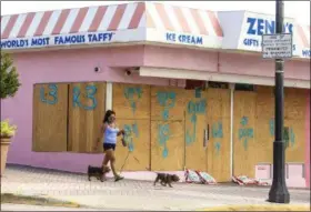  ?? JACOB LANGSTON/ ORLANDO SENTINEL VIA AP ?? Hazel Salazar walks her two small dogs past boarded up store front windows on the beach side in Daytona Beach, Fla., on Saturday as Hurricane Irma approaches.