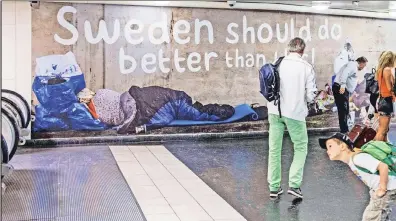  ??  ?? Not so great after all: Pedestrian­s stand near a poster showing homeless people in Stockholm, Sweden, in August. Bernie Sanders thinks America should follow the path blazed by such Scandinavi­an “utopias.”