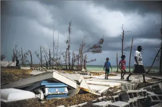  ?? Ramon Espinosa / Associated Press ?? People walk next to a shattered and waterfille­d coffin lays exposed to the elements in the aftermath of Hurricane Dorian, at the cemetery in Mclean's Town, Grand Bahama, Bahamas.