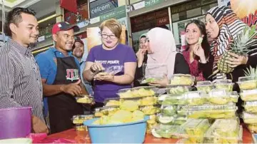  ??  ?? MOHD Idris (dua dari kiri) melayan pelanggan yang merasa buah potong yang dijualnya.