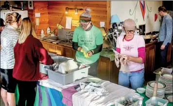  ??  ?? Becky Newell (left, in green) and Melanie Norris help clean dishes in the Headwaters School, where volunteers fed cyclists during the 12th annual Buffalo Headwaters Challenge weekend.
