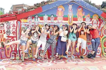  ?? — AFP photo ?? Tourists posing next to artwork by artist Huang Yung-fu, while visiting the Rainbow Village in the Nantun district of Taiwan’s central Taichung.