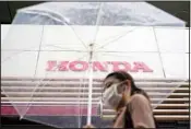  ?? ?? A woman walks in the rain near the logo of Honda Motor Company on May 13, 2022, in Tokyo. Honda’s fiscal fourth quarter profit slipped to almost half of what the Japanese automaker earned the previous year amid headwinds of supply shortages and rising raw material costs. (AP)