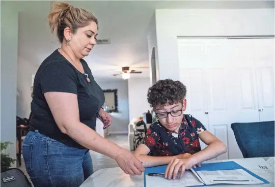  ?? PHOTOS BY JOEL ANGEL JUAREZ/THE REPUBLIC ?? Paulina Serna, left, hands her son, Luis Heberto Serna, 15, a pen as he works on his homework at his home in Phoenix.