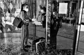  ?? AP Photo/Ashley Landis ?? Delicia Cordon receives a purchase from a sales person at Gucci on Rodeo Drive on Tuesday in Beverly Hills, Calif. The store is closed for in-store shopping, but offers curbside pickup for orders in advance.