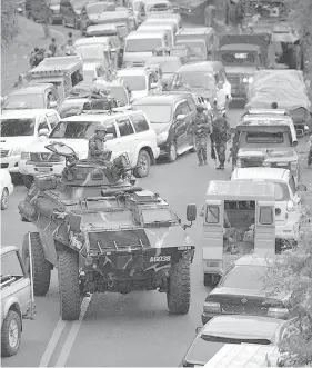  ?? AGENCE FRANCE PRESSE ?? An armored personnel carrier navigates a road congested with evacuees fleeing Marawi City on May 25, as fighting rages between government forces and Maute gunmen who have occupied some parts of the city since May 23. Security forces bombed residentia­l areas as they battled the terrorist group, which is reportedly holding hostages and murdered at least 11 civilians.