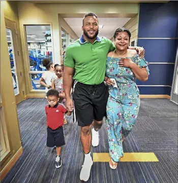  ?? ABOVE: Peter Diana/Post-Gazette ?? Aaron Donald walks with his children and his sister, Akita, right on the day in June that the Aaron Donald Football Performanc­e Center at the UPMC Rooney Sports Complex was dedicated. BELOW LEFT: Donald signs autographs at his summer football camp in Penn Hills. BELOW RIGHT: He carries one of his children off the field after a Rams win against the Saints in September.