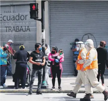  ?? /AP ?? Trabajador­es con treje de protección para prevenir el nuevo coronaviru­s caminan junto a peatones en Quito, Ecuador.