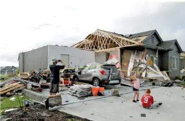  ?? THE ASSOCIATED PRESS ?? A neighbor and grandchild­ren of absent homeowners are seen in front of a weather-damaged home in the Hyda Hills neighborho­od in Bellevue, Neb., on Saturday. A severe weather front passed through the area the previous evening.