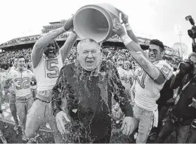  ?? Julio Cortez / Associated Press ?? North Carolina’s Patrice Rene, left, and Chazz Surratt drench coach Mack Brown after the Tar Heels routed Temple in the Military Bowl.