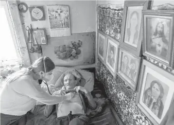  ?? EVGENIY MALOLETKA/AP ?? Wearing a face mask to guard against the coronaviru­s, Dr. Viktoria Mahnych checks on a COVID-19 patient Jan. 6 at his home in Ivano-Frankivsk, Ukraine. To date, more than 21,000 Ukrainians have died from COVID-19.