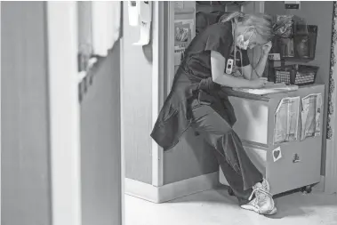  ?? MYKAL MCELDOWNEY/INDYSTAR ?? Tired, a nurse sits propped against a wall inside Franciscan Health’s critical care unit. She fills out paperwork as fellow nurses and doctors make their rounds, Sept. 20.