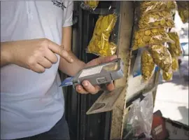  ??  ?? A STREET VENDOR uses a card reader Thursday in Caracas, Venezuela. The once-prosperous nation, enmeshed in political and economic turmoil, has grappled with hyperinfla­tion and a consequent shortage of cash.