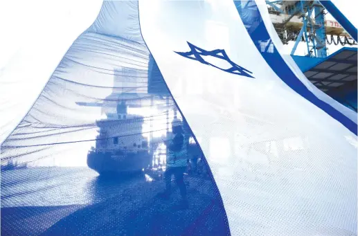  ?? (Amir Cohen/Reuters) ?? A WORKER at the sea port of Ashdod coordinate­s a crane to hang a giant Israeli national flag ahead of Remembranc­e Day.