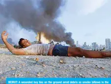  ??  ?? BEIRUT: A wounded boy lies on the ground amid debris as smoke billows in the background at the scene of a massive explosion that hit the port of Beirut in the heart of the Lebanese capital on August 4, 2020.