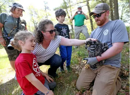  ?? ?? State Sen. Becca Rausch of Needham, Mass., pats the bald eagle chick with her children, Eitan Barnoon, 8, and Micah Barnoon, 6, after it was tagged by Fleming and Wright.