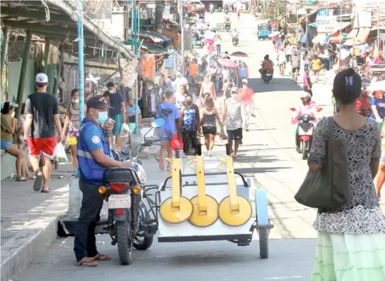  ?? EMERITO ANTONIO/POND NEWS ASIA ?? USING a megaphone, a barangay officer reminds residents and passersby to use their masks and shields properly at a public market in Dasmariñas Cavite.