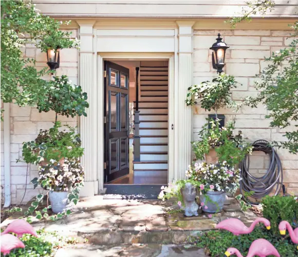  ??  ?? The delicate leaves and flowers of potted flowering plants create a perfect balance with the architectu­ral molding and a dramatic black front door.