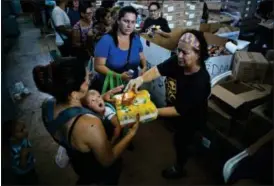  ?? RAMON ESPINOSA — THE ASSOCIATED PRESS ?? Awoman with her child receives free diapers and shower gel, as she and others line up for food and other donated staples from the MARC Ministry, a non-profit charity in Manati, Puerto Rico. Charity workers say most of the needy who come to them are ill pensioners, seniors, students and the unemployed.