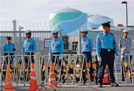  ?? FOTO: AFP ?? Streng bewacht von Polizisten schließt Japan in Kagoshima wieder den ersten Meiler seit dem Gau von Fukushima ans Stromnetz an.
