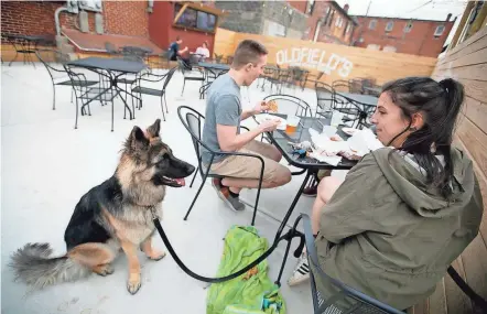  ?? PHOTOS BY COURTNEY HERGESHEIM­ER/COLUMBUS DISPATCH ?? Molly Radigan, with her dog Madden, Josh Rivera and Craig Yantko, not pictured, share beer and pizza on the expanded patio at Oldfield's North Fourth Tavern on Tuesday.