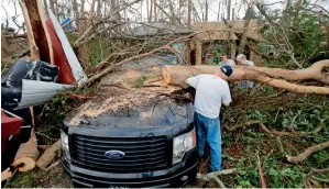  ?? AP ?? People cut away a tree that fell on a vehicle in the aftermath of Hurricane Michael in Panama City. —