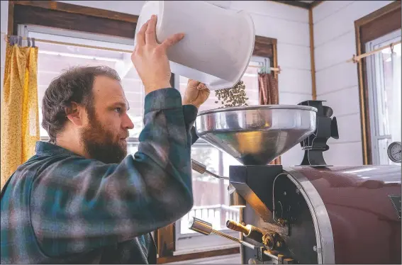  ?? (Globe-Gazette/Chris Zoeller ?? Erik Johnson loads his coffee bean roaster with a batch of raw Tanzania peaberry beans in his roasting studio at his home in Waverly, Iowa.