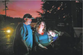  ?? Gabrielle Lurie / The Chronicle ?? Aaron Johnson, wife Tammy White and daughter Leah Johnson, 11, sit outside their house without electricit­y Thursday as they watch news on their phone for updates about the nearby Kincade Fire.