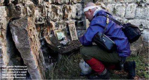  ??  ?? Aleksander Malkhasyan lights some incense and says a prayer at a small mountainsi­de shrine in Ijevan State Sanctuary