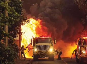  ?? Firefighte­r saves an American California. — AFP photo ?? A flag as flames consume a home during the Dixie fire in Greenville,