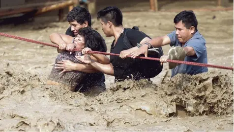  ?? Foto: Martin Mejia, dpa ?? Schlamm und Wassermass­en rauschen durch die Straßen der peruanisch­en Hauptstadt Lima. Diese Menschen versuchen, die Fahrbahn an einem Seil zu überqueren. Nicht alle entkommen dem Schlamm. Doch es gibt auch kleine Wunder.