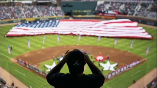  ?? ASSOCIATED PRESS ?? A spectator takes a photo of a United States flag as it is unveiled for the national anthem as part of Military Appreciati­on Day before a baseball game between the Atlanta Braves and the Washington Nationals in Atlanta. The anthem has been a standard...