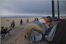  ?? JAE C. HONG — THE ASSOCIATED PRESS FILE ?? People ride their bikes past a homeless encampment set up along the boardwalk in the Venice neighborho­od of Los Angeles.