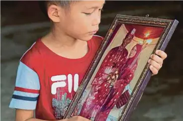  ?? PIC BY ABDULLAH YUSOF ?? Ahmad Faqih Nazmi Ahmad Faizal clinging to a photo of his late parents in Taman Kaya, Taiping, on Tuesday.