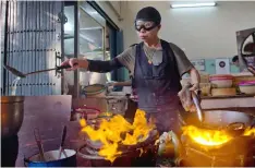  ?? GEMUNU AMARASINGH­E/AP PHOTOS ?? Thai cook Supinya Jansuta, 72, better known as “Jay Fai,” wearing goggles, cooks with two flaming woks at her eatery in Bangkok, Thailand. After spending more than three decades cooking in an unassuming outdoor kitchen, Jay Fay has been propelled to...