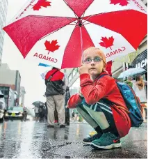  ?? JOHN MAHONEY/MONTREAL GAZETTE ?? Ian Jones squats under an umbrella as he watches the Canada Day parade on Ste-Catherine St. on Wednesday. Jones and his family are visiting from Cleveland.