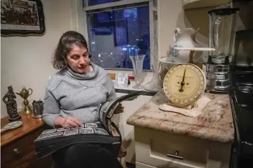  ?? (AP Photo/bebeto Matthews) ?? Anne D'innocenzio, above, scrolls through a family album inside her kitchen, surrounded by mementos from her childhood home, including a working blender from the 1960s and an old food scale from the 1940s, Monday, Feb. 26, in New York. It's been eight months since she closed the door for the last time to her childhood home in suburban New Jersey and said goodbye to more than a half century of memories.
