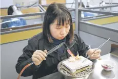  ?? ?? A jewellery cra swoman heating a gold flower to shape the petals at a master studio in Foshan.